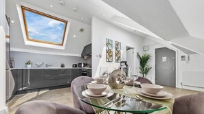 A modern kitchen with a skylight, a dining area with a glass table, and a grey door. - Flat -12 (London)