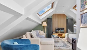 Un ambient modern d'estil loft amb un sostre inclinat, una biblioteca integrada, un sofà, un butaca blava i una làmpada de peu.
