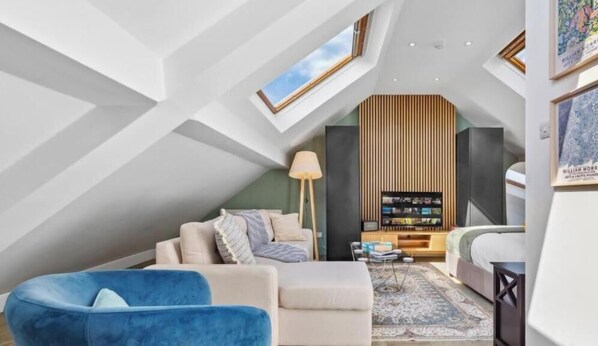 Ein modernes Loft mit schrägem Dach, einer integrierten Bücherwand, einem Sofa, einem blauen Sessel und einer Stehlampe.