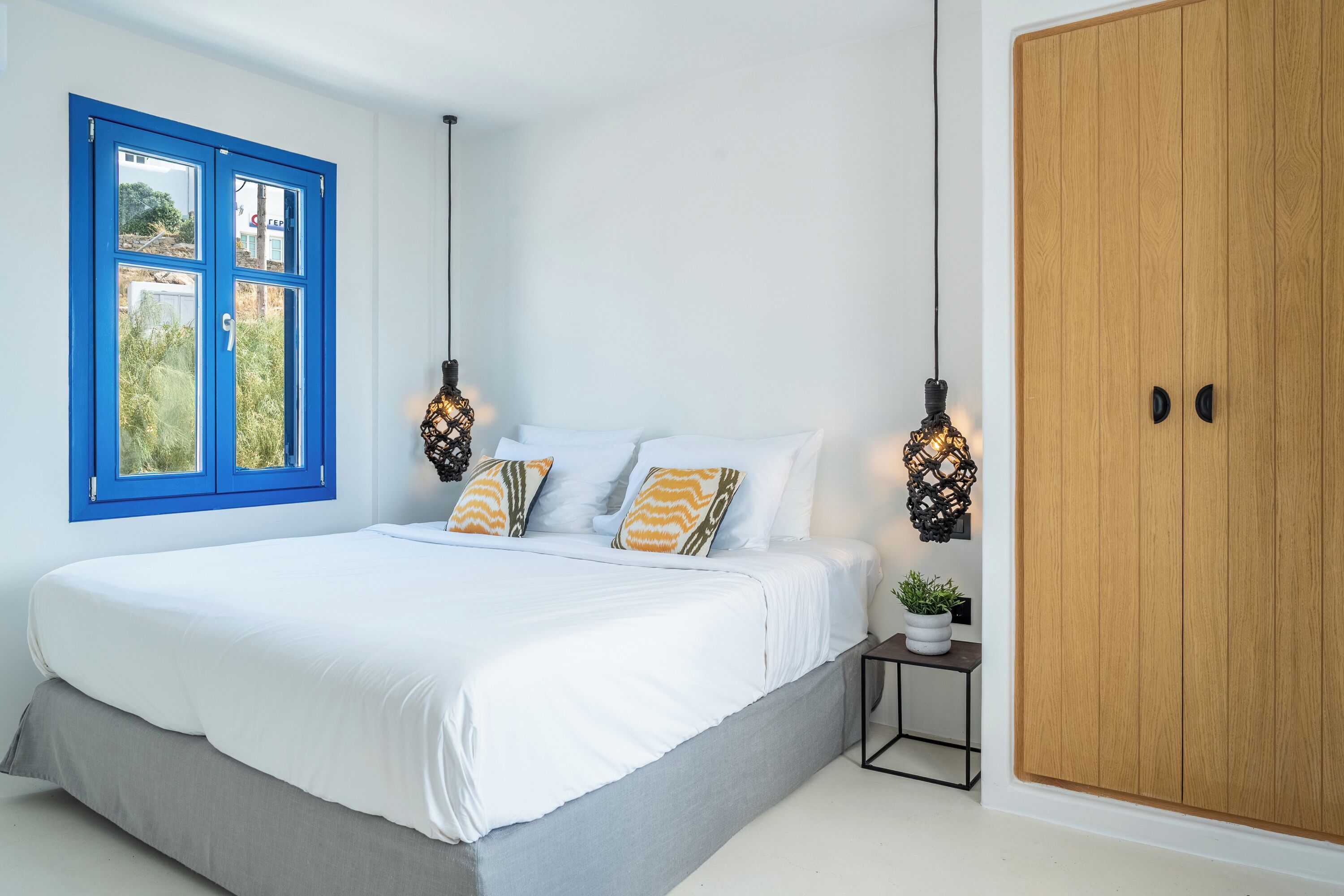 Quarto com cama, janela, guarda-roupa e mesa de cabeceira com uma planta.