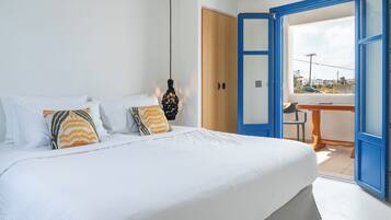 A bedroom with a bed, pillows, a hanging light fixture, a wooden door, and a view through an open door.