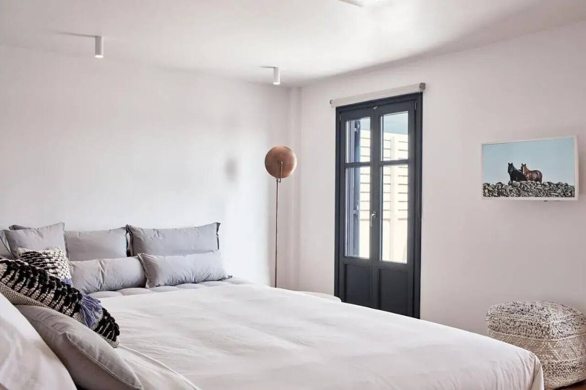 Une chambre à coucher avec un lit, des oreillers, une lampe sur pied, une fenêtre et un tableau accroché au mur.