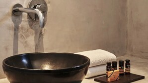 Une salle de bain avec un miroir rond, une porte bleue, un lavabo noir et une serviette.