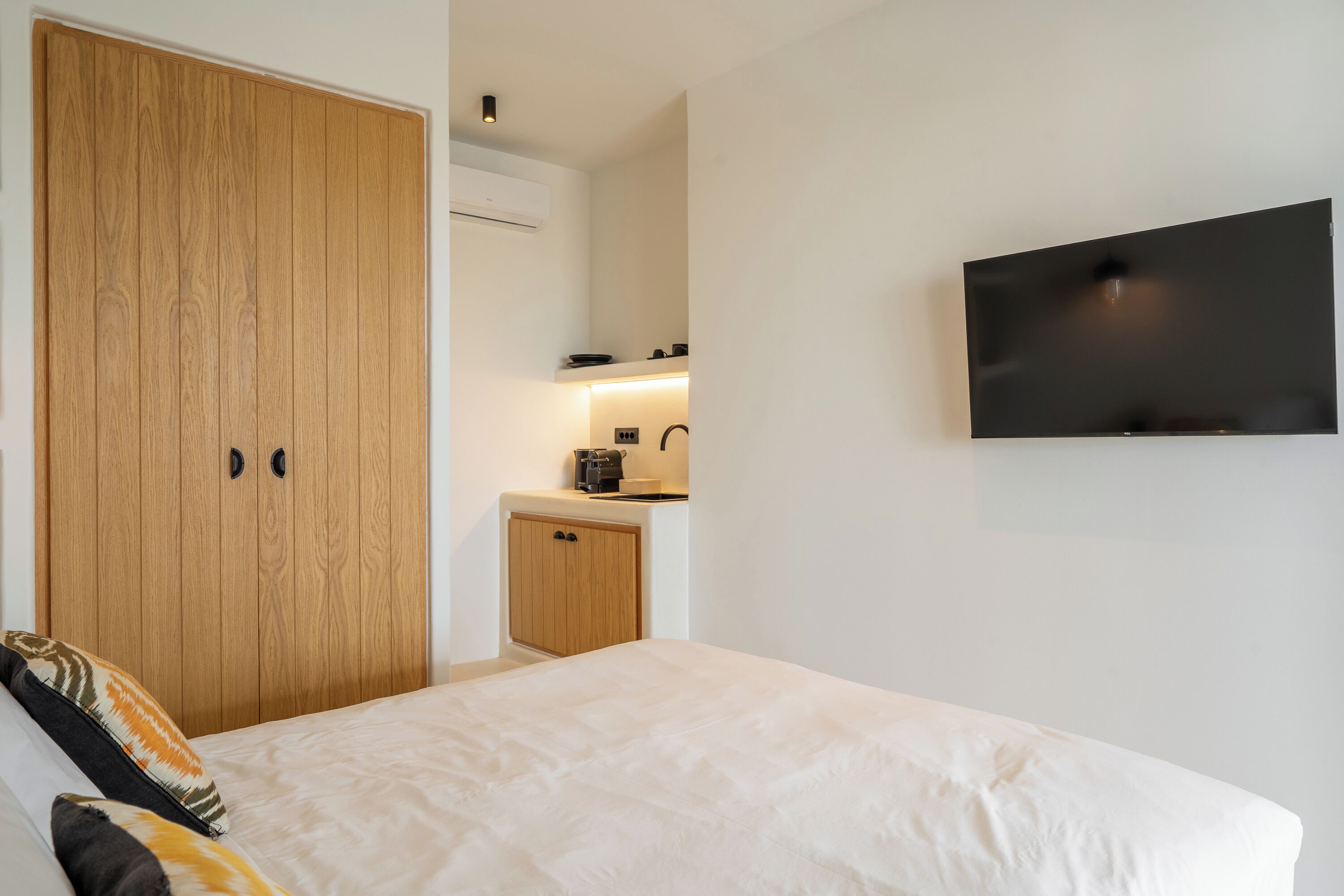 Un dormitorio con cama, armario de madera, kitchenette y televisor en la pared.