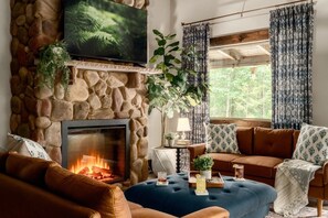 A cozy living room with a stone fireplace, a television mounted above it, and a comfortable seating area with a sofa and ottoman. - Hot Tub/Fire Pit/Game Room/Secluded - Blue Bird (Sevierville)