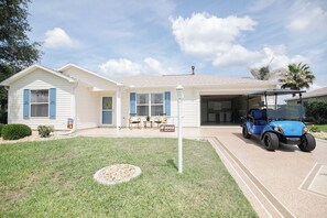 Una casa a un piano con garage, prato e un golf cart parcheggiato davanti.