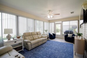Een ruime woonkamer met een beige bank, een blauwe fauteuil, een salontafel en een bijzettafeltje met een lamp.