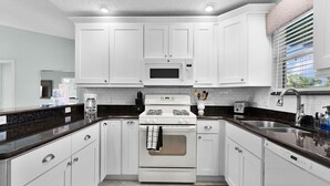 Une cuisine moderne avec des meubles blancs, un four à micro-ondes encastré, une cuisinière et un évier.