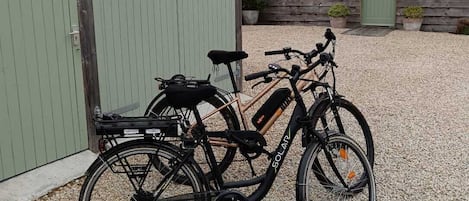 Two bicycles parked on gravel, a green building with windows, and a wooden structure with a door.