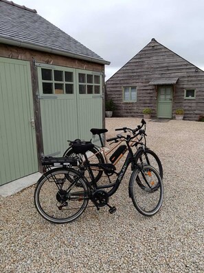 Two bicycles parked on gravel, a green building with windows, and a wooden structure with a door.
