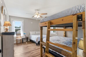 A bunk bed room with a ceiling fan, a desk with a lamp, and a window with curtains. - WV68: Sand Dollar Cottage | Centrally Located | Pool Access (Ocracoke)