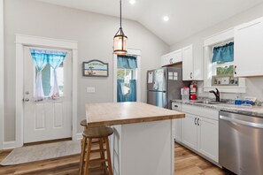 Una cocina con una isla central, electrodomésticos de acero inoxidable y una lámpara colgante.
