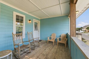 Eine Veranda mit Holzschaukelstühlen, einem kleinen Tisch und einer Tür mit Fenster.