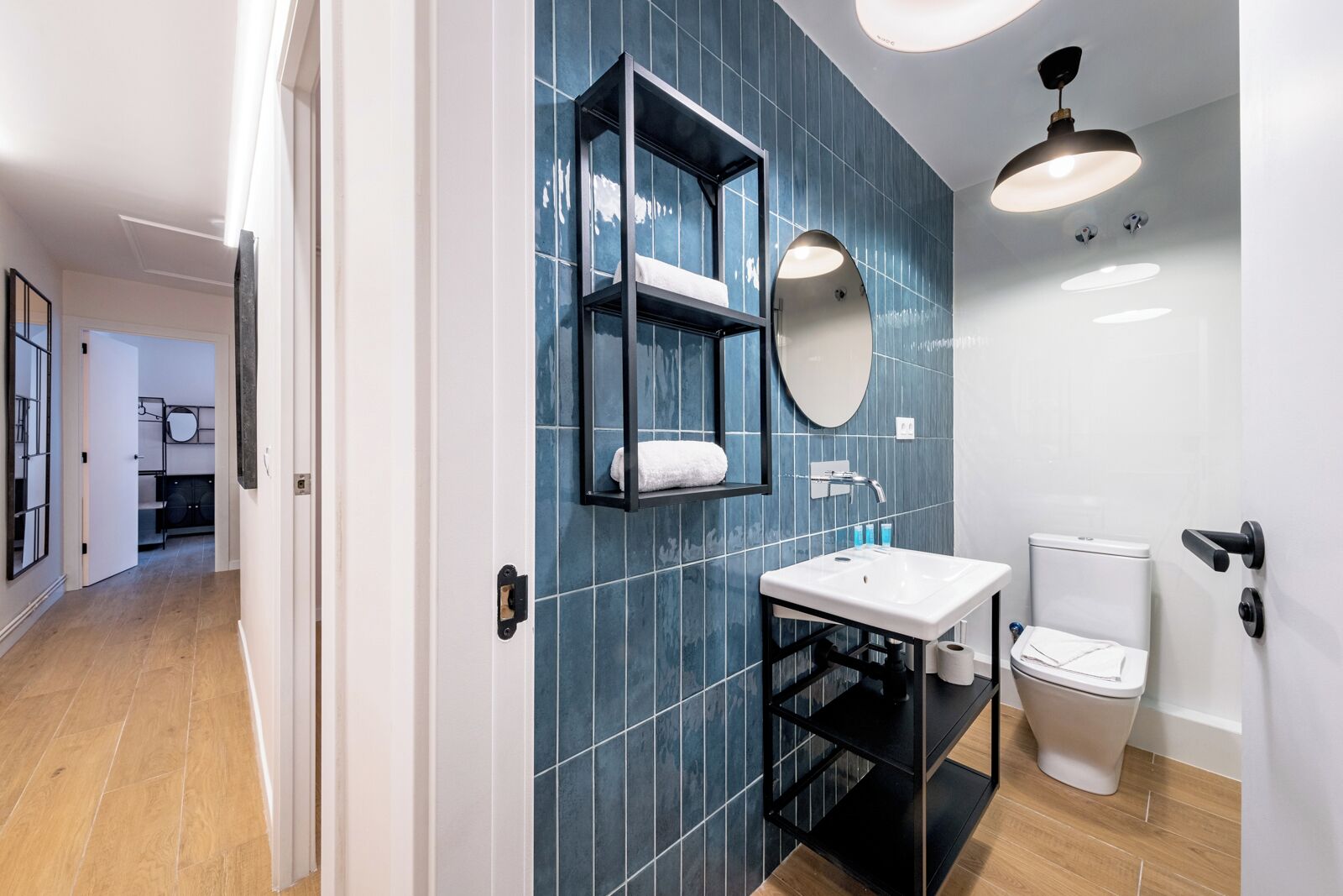A modern bathroom with a white sink, a black vanity, a round mirror, and a toilet.