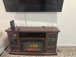 Een houten entertainmentkast met een open haard, een aan de muur bevestigde televisie en een afstandsbediening op de kast.