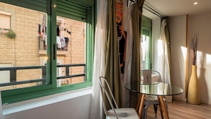 Ein Zimmer mit Glastisch, einem Sessel, einem Fenster mit Blick auf ein Gebäude und einer Vase mit Zweigen.