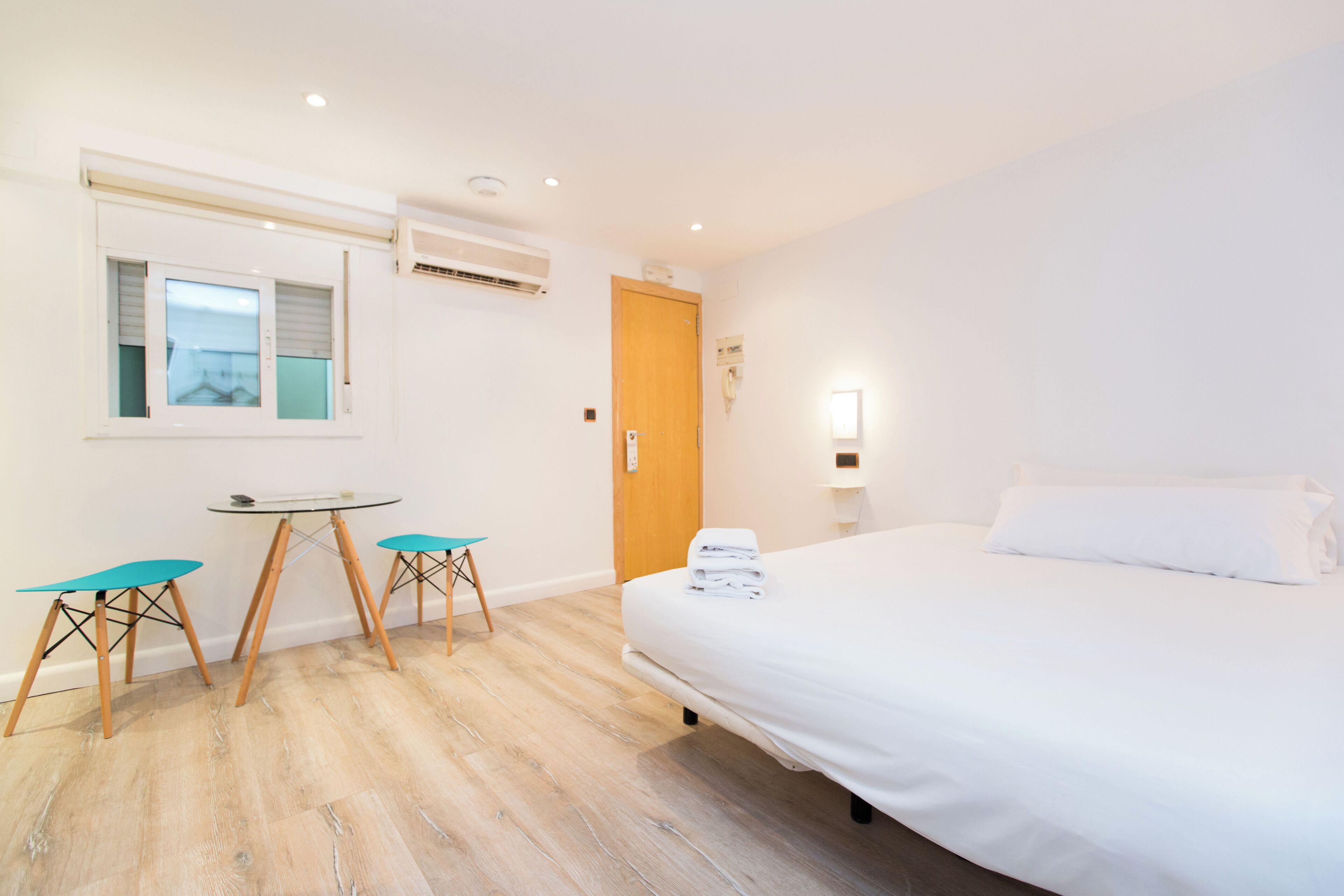 Habitación de hotel con cama, escritorio y dos sillas, ventana y aire acondicionado.