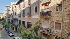 A multi-story building with balconies, a narrow street, and parked cars. - Ample Bolsa estándar tipo 1 (Barcelona)