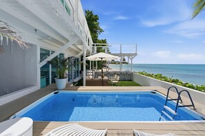 Ein Poolbereich mit Blick auf den Ozean, eine überdachte Sitzgelegenheit und ein Gebäude mit großen Fenstern.