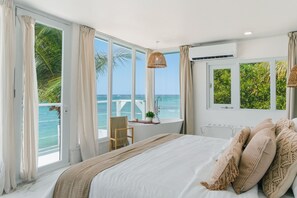 Ein Schlafzimmer mit einem großen Bett, Meerblick, einem Fenster mit Vorhängen und einem Sessel am Fenster.