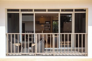 Ein Balkon mit Korbmöbeln, eine Glastür, die zum Küchenbereich führt, und Blick ins Grüne.