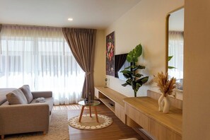 Ein modernes Wohnzimmer mit einer Couch, einem runden Glastisch, einer großen Pflanze, einem Spiegel und einem Holztischchen.