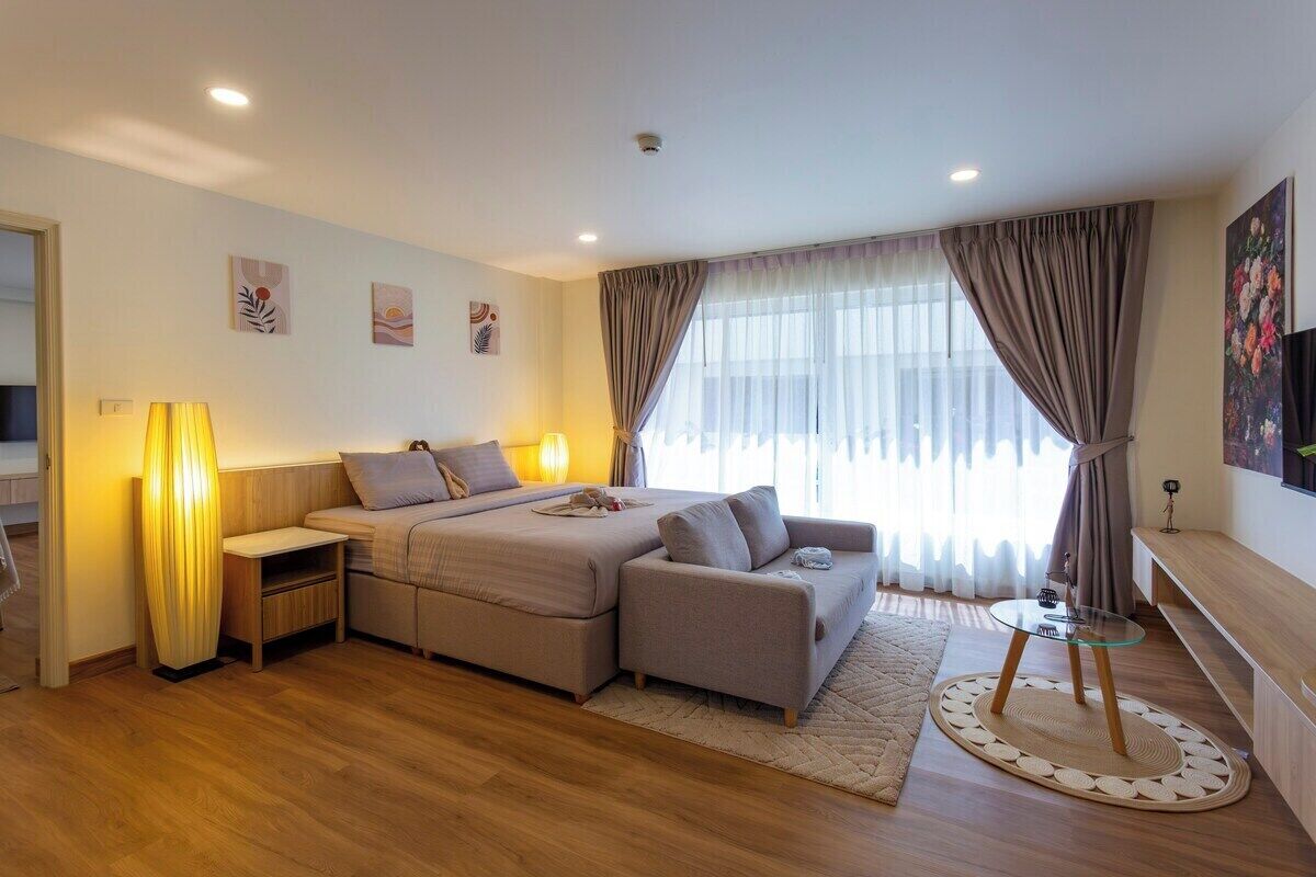 Une chambre d’hôtel moderne, équipée d’un lit, d’un canapé, de tables de chevet, d’une table basse en verre et d’une grande fenêtre avec des rideaux.