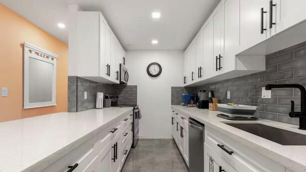 Una cucina moderna con mobili bianchi, uno schienale grigio e un'isola centrale con un lavello.