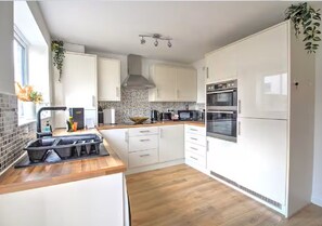 Eine moderne Küche mit weißen Schränken, einer Holz Arbeitsplatte, einem eingebauten Backofen und einer Spritzschutzwand.