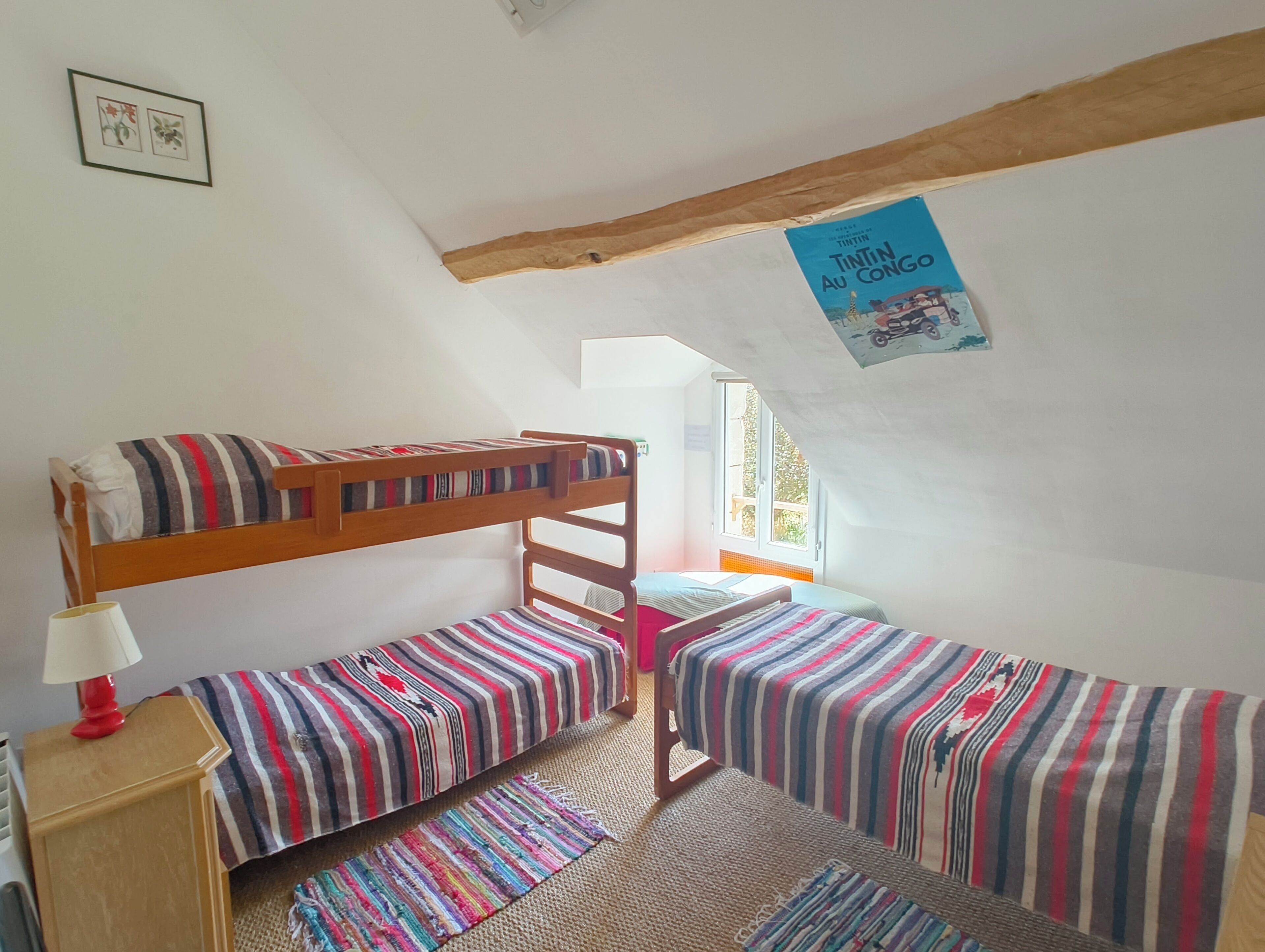A dormitory room with bunk beds, a small desk, a lamp, and a poster on the wall.