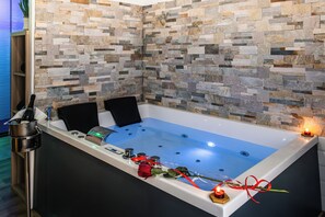 Una vasca da bagno con parete in mosaico di pietra, una rosa e delle candele.