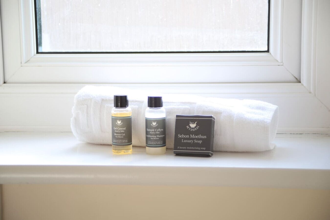 A window sill with three toiletry items: a shower gel, a conditioning shampoo, and a luxury soap.