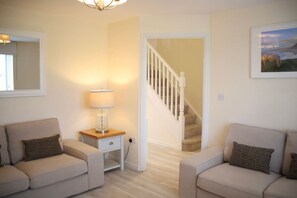 A living room with two sofas, a lamp, a staircase, and a framed picture on the wall. - Cosy pet friendly family home with coastal views (Sir Gaerfyrddin)