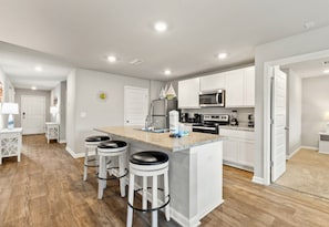A modern kitchen with white cabinets, a granite countertop, and a central island with stools. - Coastal Retreat Near Gulf Shores & Orange Beach (Foley)