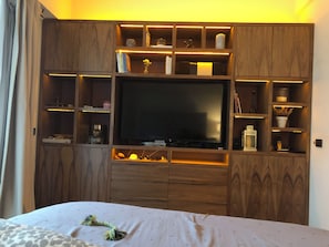 Ein Schlafzimmer mit einem Bett, einem Fernseher und Holzregalen mit verschiedenen Gegenständen.