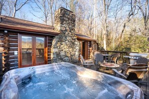 A log cabin with a stone chimney, a hot tub, outdoor seating, and a grill. - Buckhorn Hideaway (Gatlinburg)