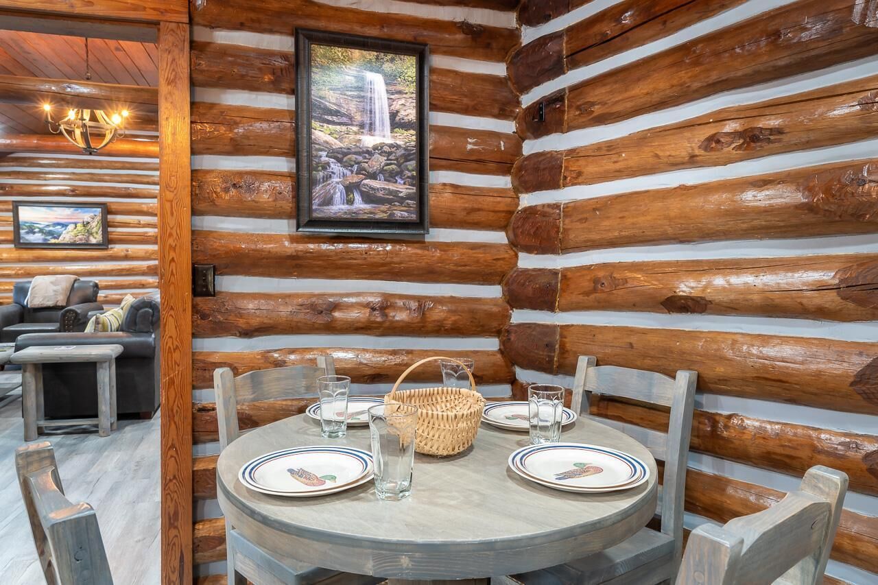 L’intérieur d’une cabane en rondins, avec une table à manger dressée pour quatre personnes, une cheminée et un tableau encadré représentant une cascade.