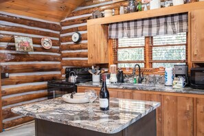 A kitchen with wooden walls, a marble countertop, a wine bottle, and a clock. - Buckhorn Hideaway (Gatlinburg)