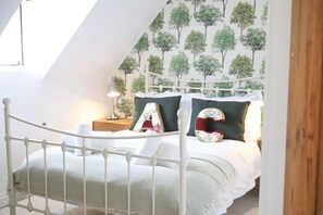 Ein Schlafzimmer mit einem weißen Metallbettgestell, einer grün gemusterten Bettdecke und einer Wand mit Baumtapete.