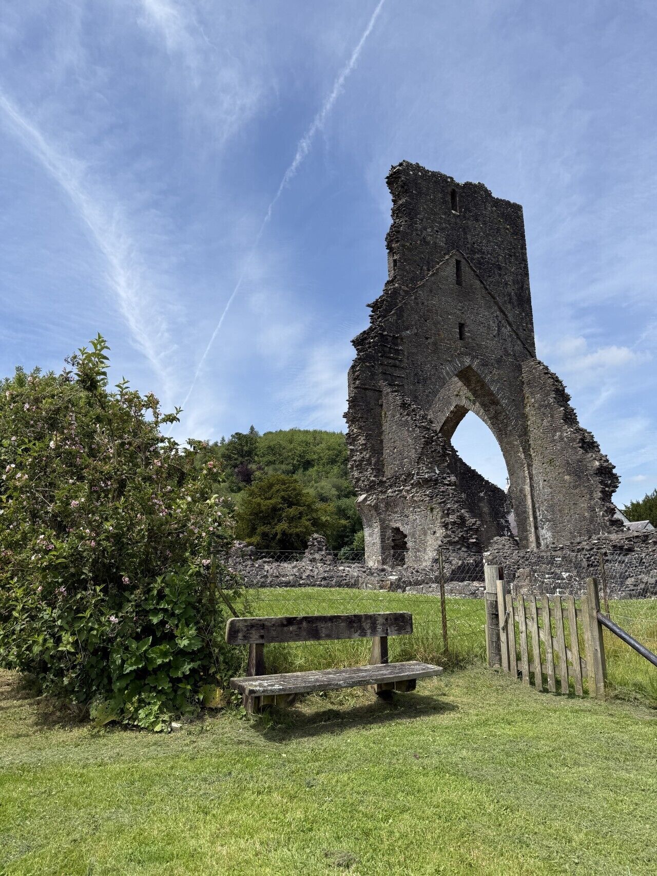 A historical stone structure with an arch, surrounded by greenery and a wooden bench.