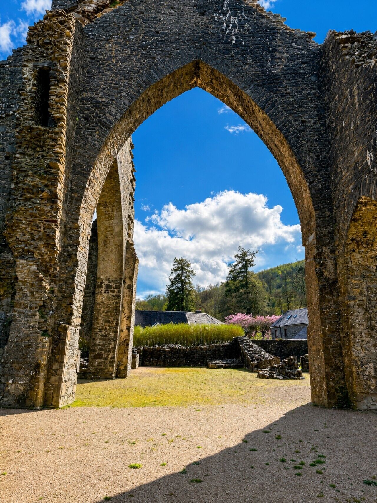 An ancient stone archway leading to a grassy area with a clear sky and trees in the background.