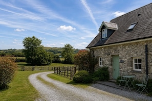 Ein Steinhaus mit Kiesweg, Holzzaun und Blick ins Grüne.