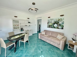 A dining area with a table and chairs, a sofa, and a painting on the wall. - The Marilena Penthouse (Capri)
