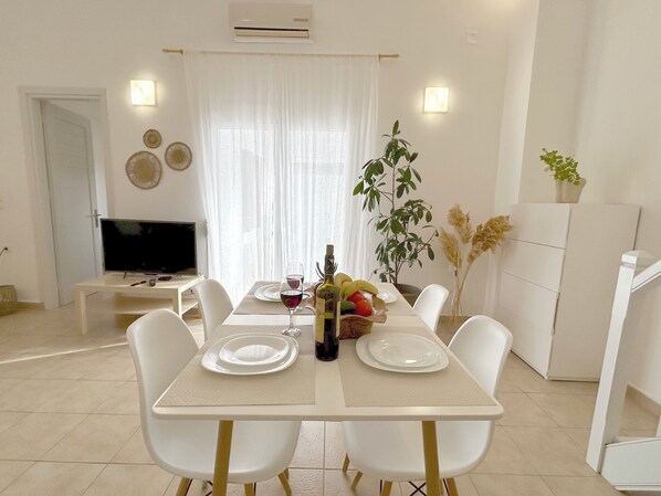 Un coin repas avec une table mise pour deux personnes, un téléviseur et une plante.