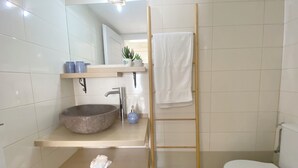 Een badkamer met een houten ladder, een wit toilet, een rond wastafeltje en een plank met toiletartikelen.