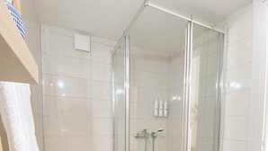 Een moderne badkamer met een douchecabine, witte tegels, een toilet en twee potplanten.