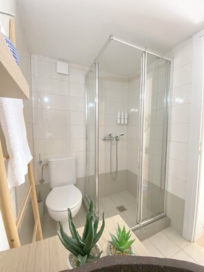 Et moderne badeværelse med et brusebad i glas, hvide fliser, et toilet og to krukker med planter.