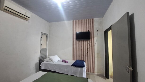 Une petite chambre avec un lit simple, un téléviseur fixé au mur, une porte et un appareil de climatisation.