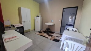 A compact kitchen with a refrigerator, a sink, a small stool, and a dining area with a table and chairs.