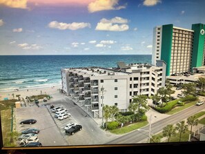 Ein mehrstöckiges Hotel mit Parkplatz, Blick auf den Strand und einem Gebäude mit grüner Fassade.